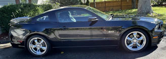 Side view of a sleek black car with spotless windows and polished rims parked outside a modern home