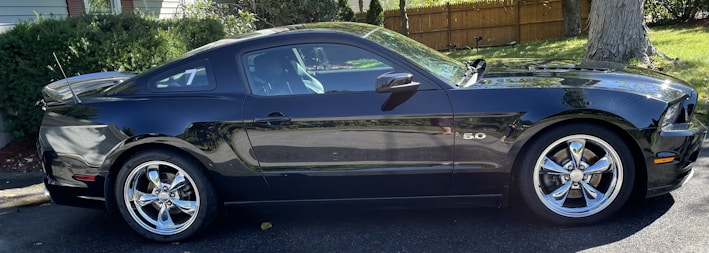 A sleek black car with custom wheels parked on a city street.