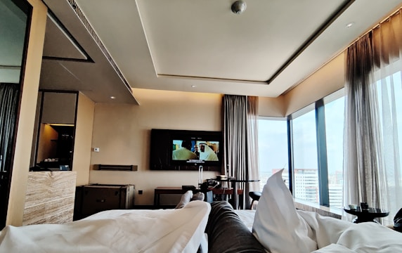 Cozy hotel room with a large window overlooking a bustling cityscape at dusk.