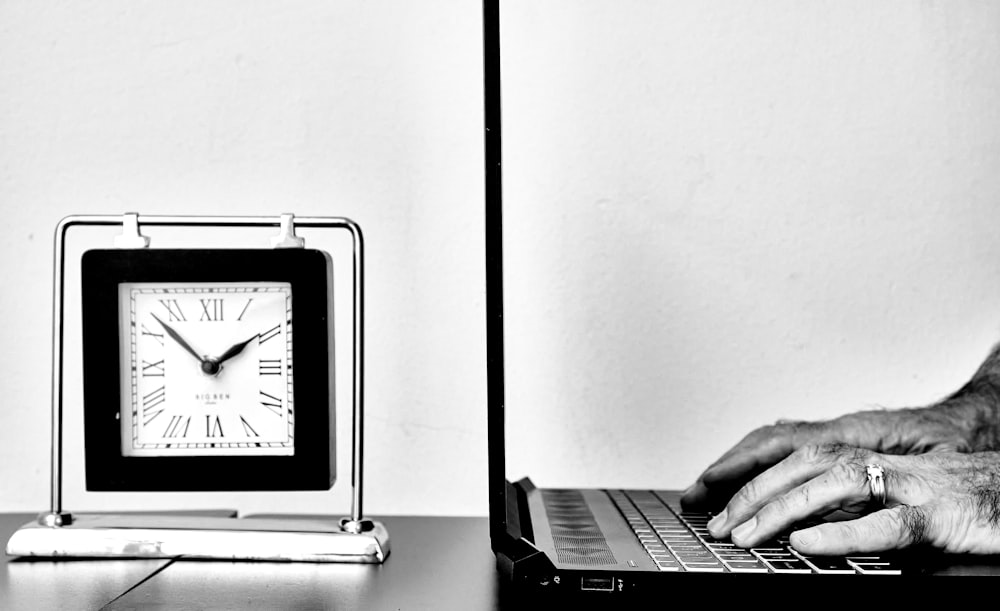 a person typing on a laptop next to a clock