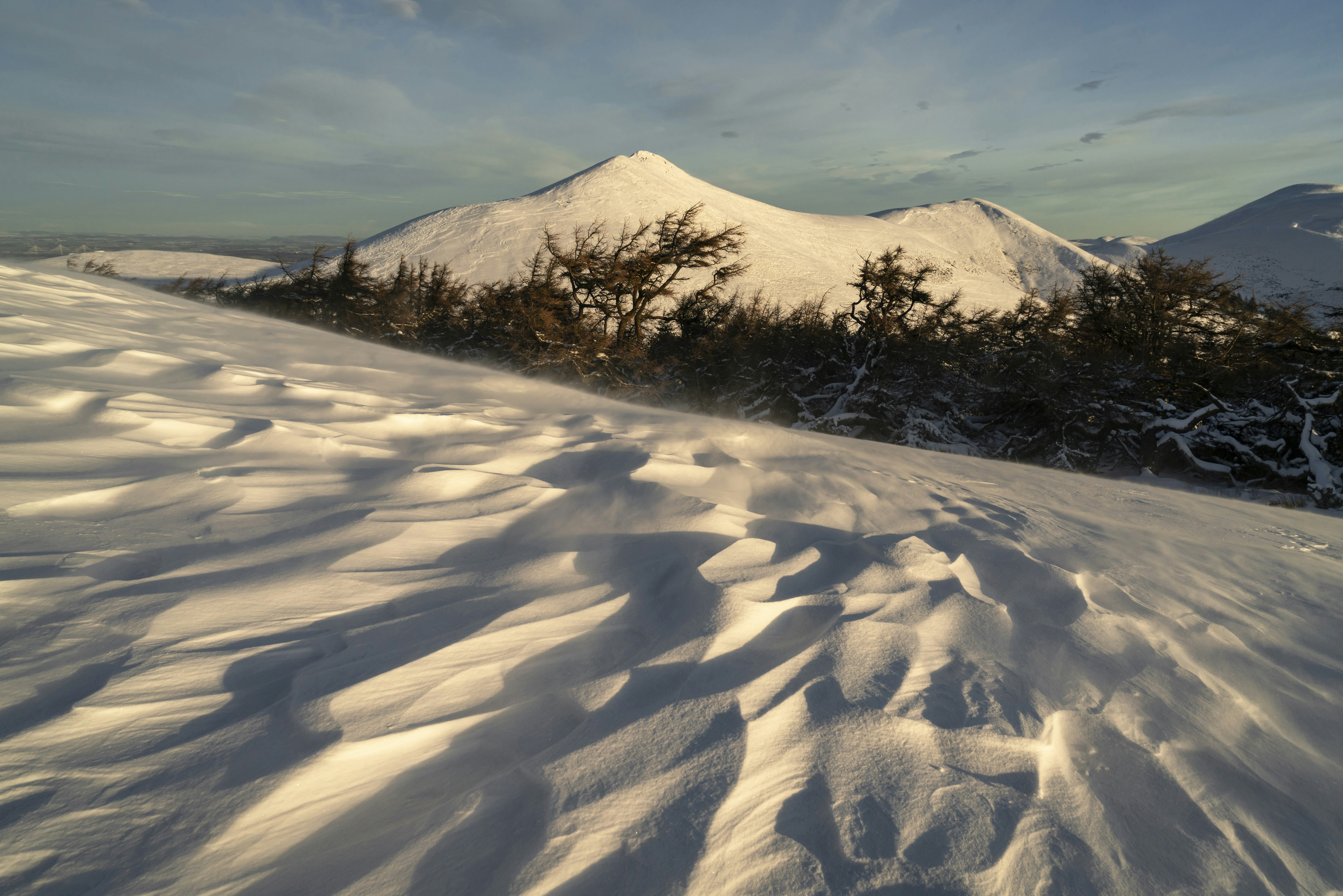 a snow covered hill with trees and mountains in the background