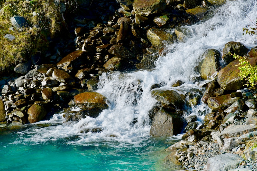 a stream of water running over rocks into a blue pool
