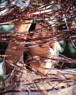 A person is joyfully surrounded by shiny, metallic streamers that reflect sunlight. Their face and hands are partially visible through the intricate tangle of ribbons, adding a dynamic and playful feeling to the scene.
