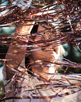A person is joyfully surrounded by shiny, metallic streamers that reflect sunlight. Their face and hands are partially visible through the intricate tangle of ribbons, adding a dynamic and playful feeling to the scene.