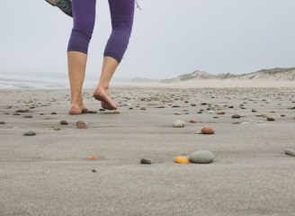 a woman walking across a sandy beach next to rocks