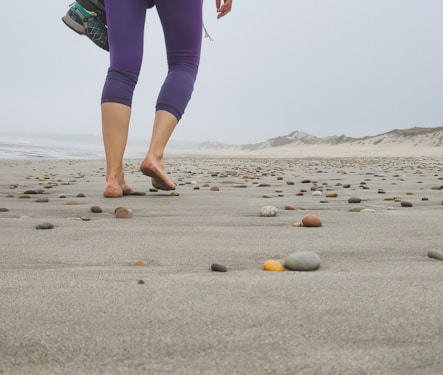 a woman walking across a sandy beach next to rocks