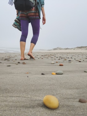 a woman walking across a sandy beach next to rocks