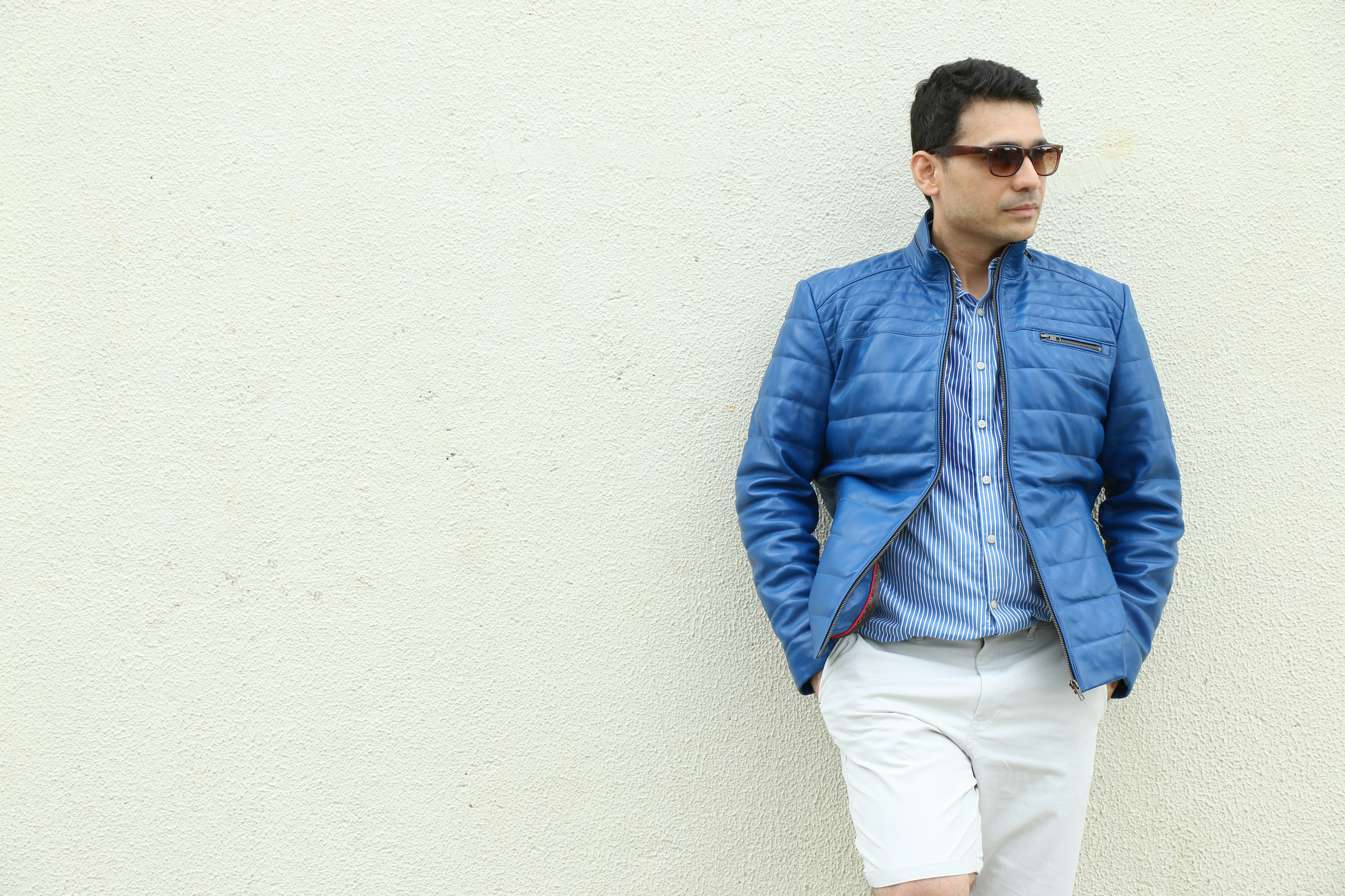 a man in a blue jacket leaning against a white wall