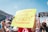 A group of people participating in a protest, holding various signs advocating for women's rights and bodily autonomy. The central sign, written in bold on bright yellow paper, says 'Our Daughters Deserve Choices.' Other visible signs include messages like 'Bans Off My Body' and 'Keep Your Laws Off My Body.' Many participants are wearing masks, and it appears to be daytime with a clear blue sky.