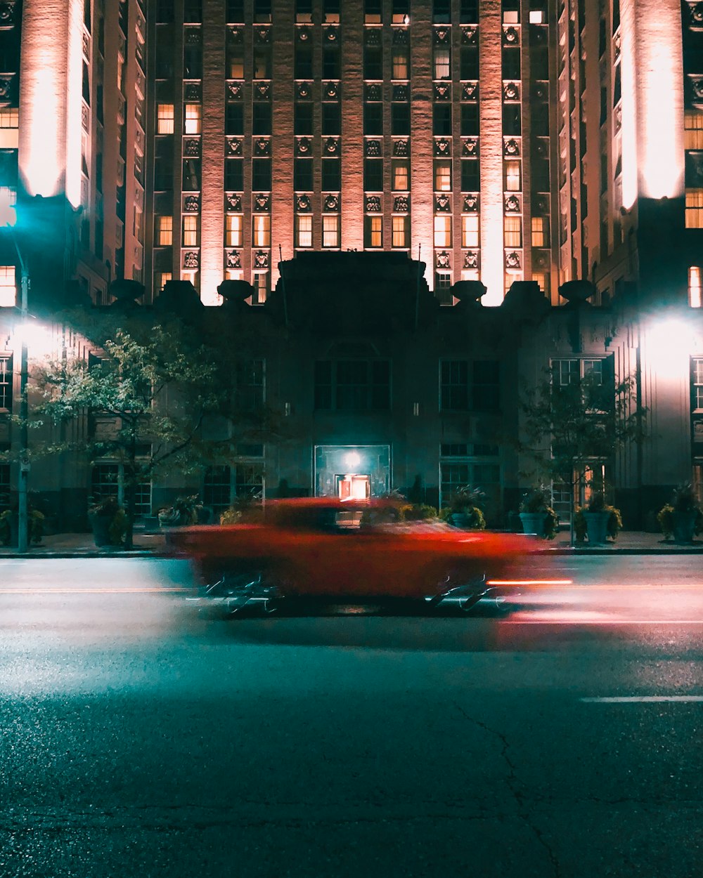 a red car driving down a city street at night