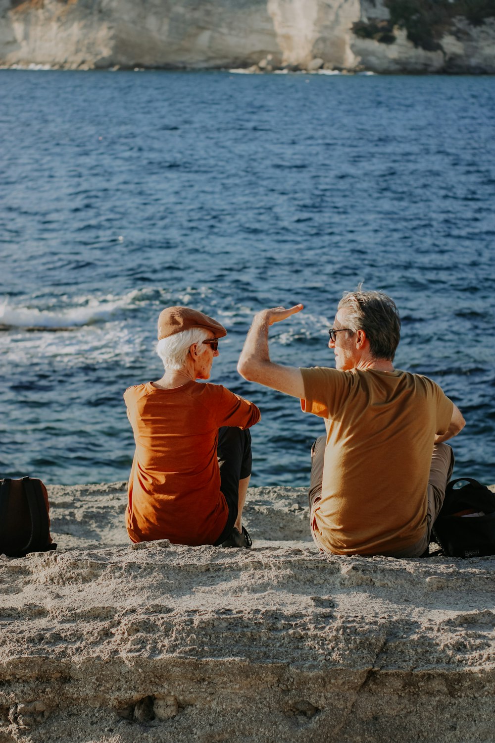 a man and a woman sitting on a beach next to a body of water