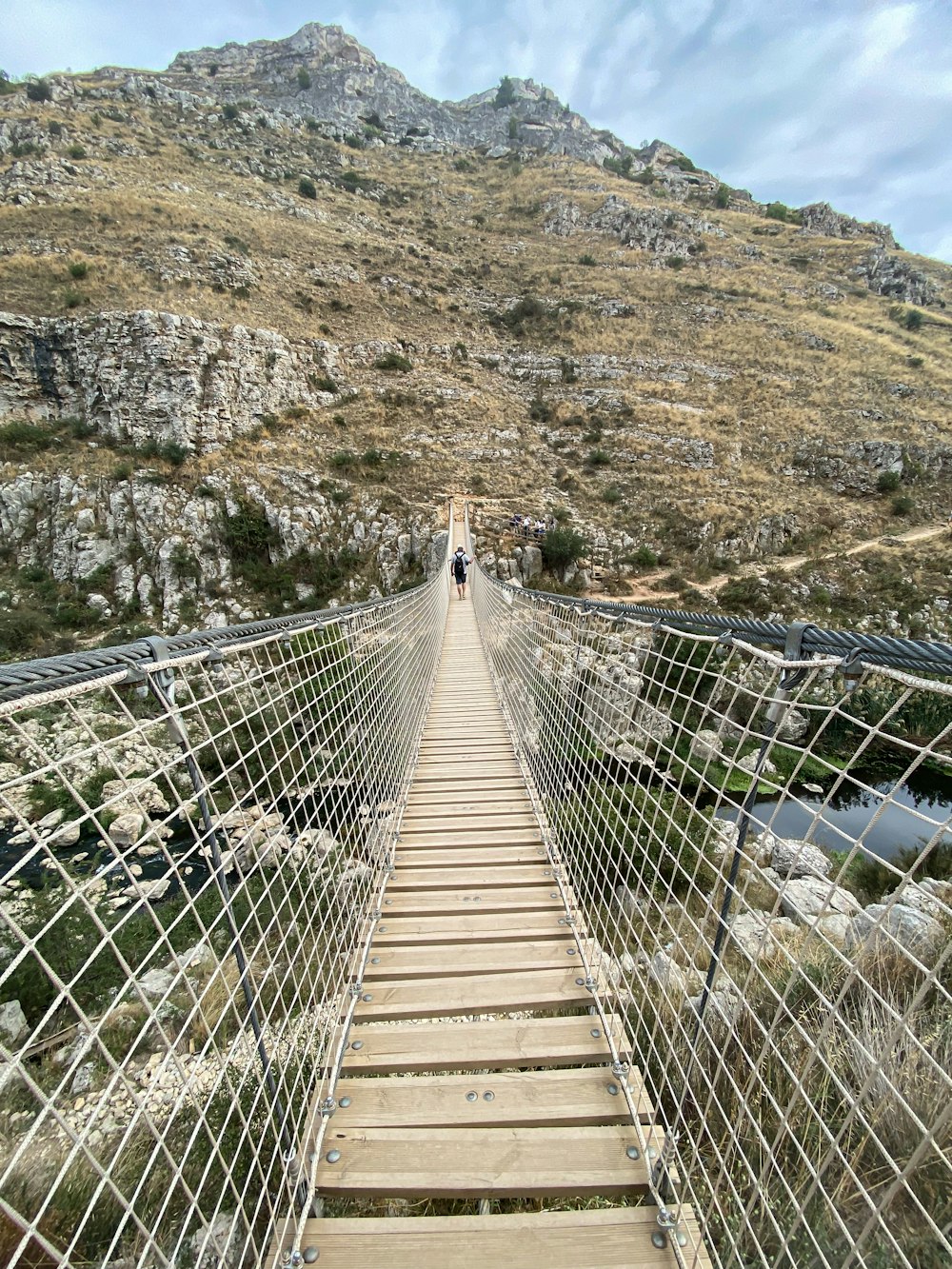 a man walking across a suspension bridge over a river