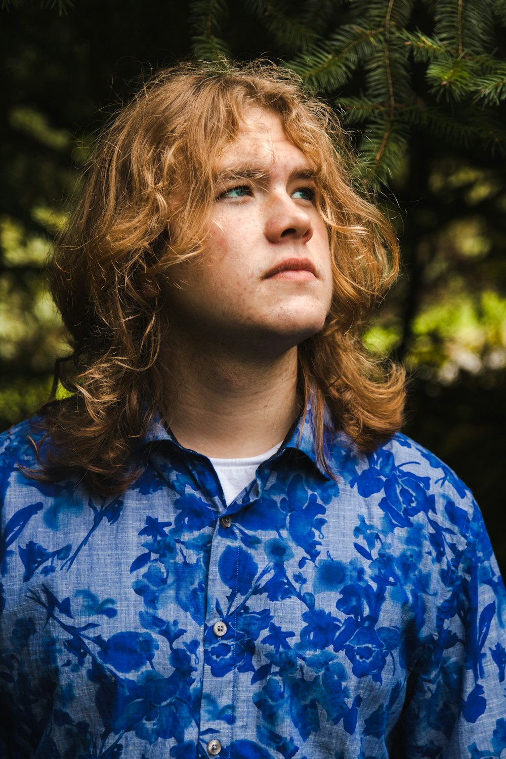 a man with long hair standing in front of a tree