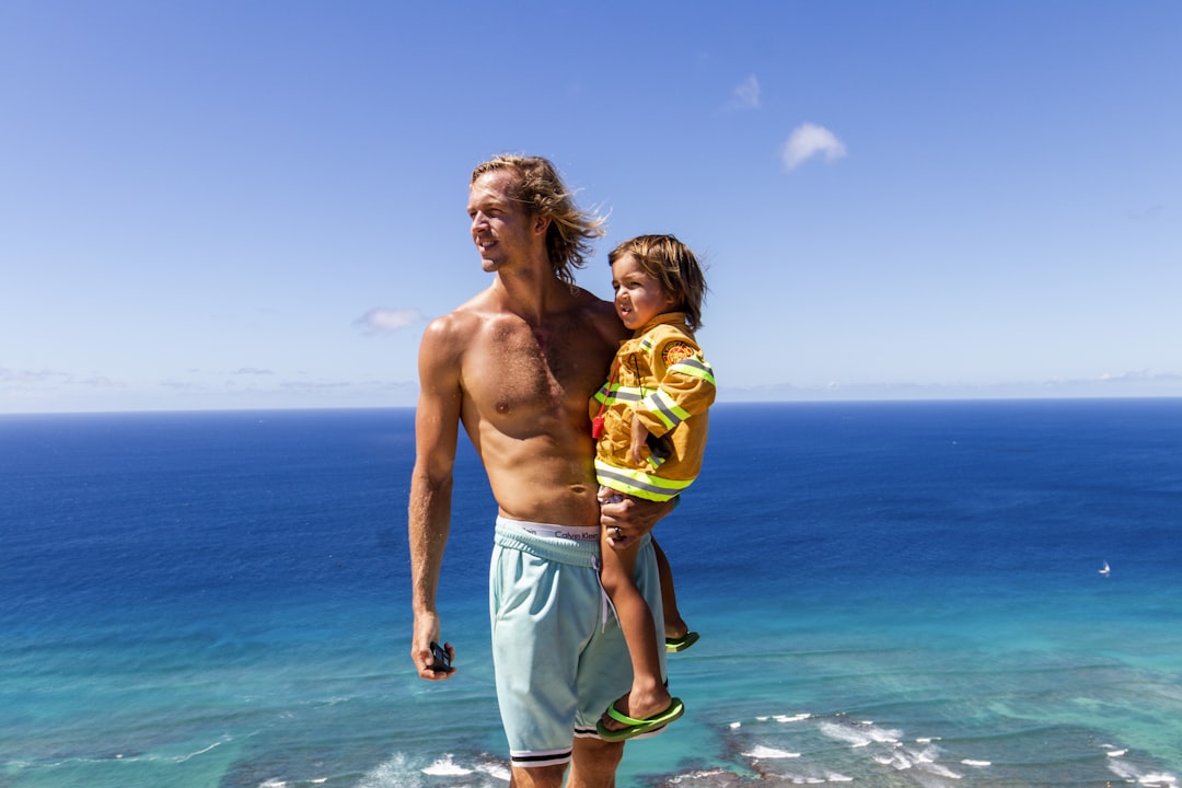 a man and a child standing on a cliff overlooking the ocean,