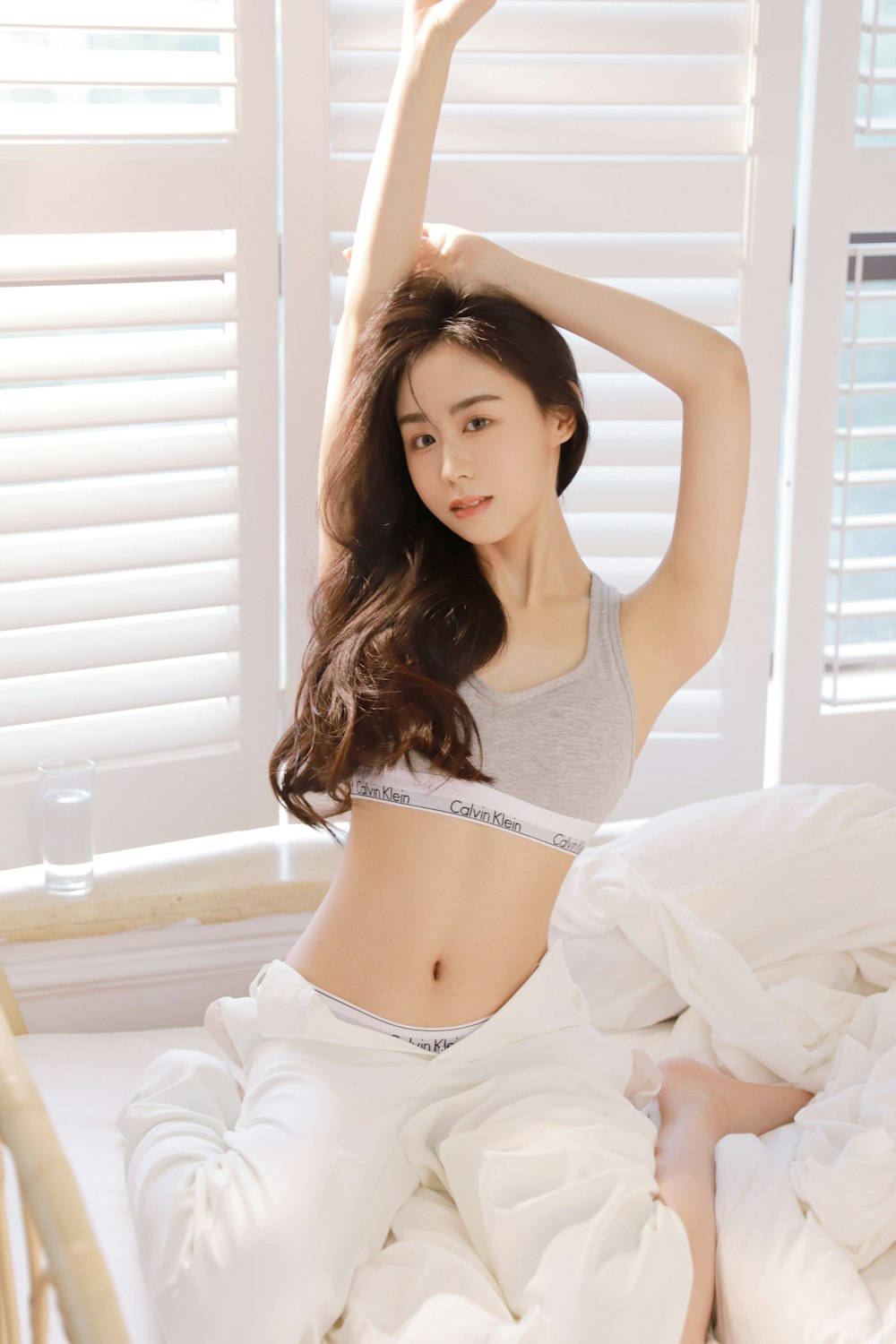 a woman in a gray top and white pants sitting on a bed