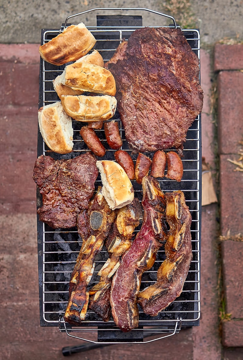 Beef short ribs, chorizo and bread rolls grilling together over hot coals