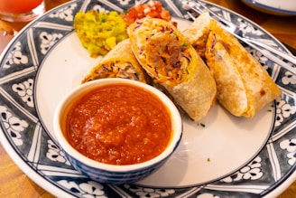 A steaming hot costilla burrito wrapped in foil, with a side of spicy salsa roja.