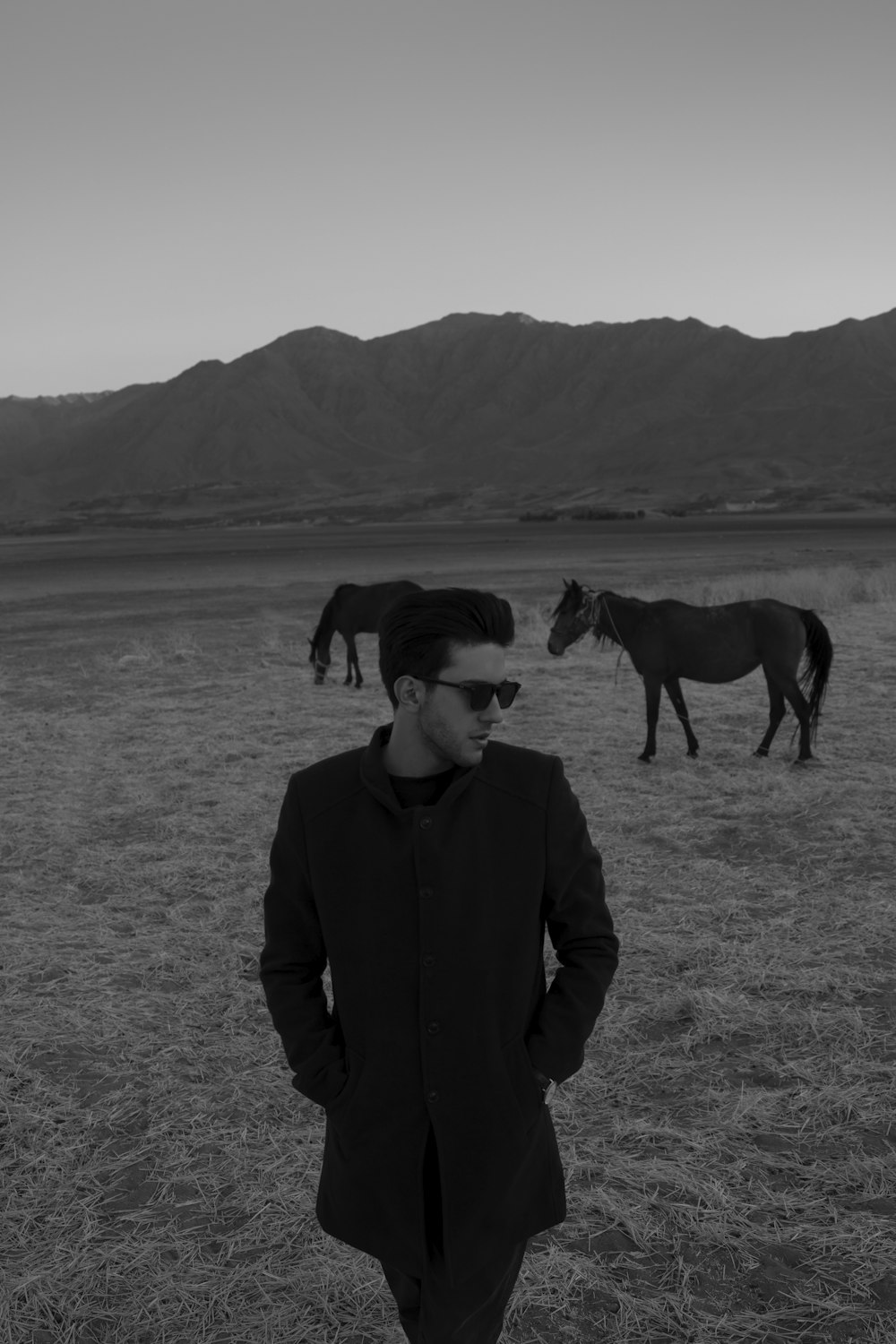 a man standing in a field with horses in the background