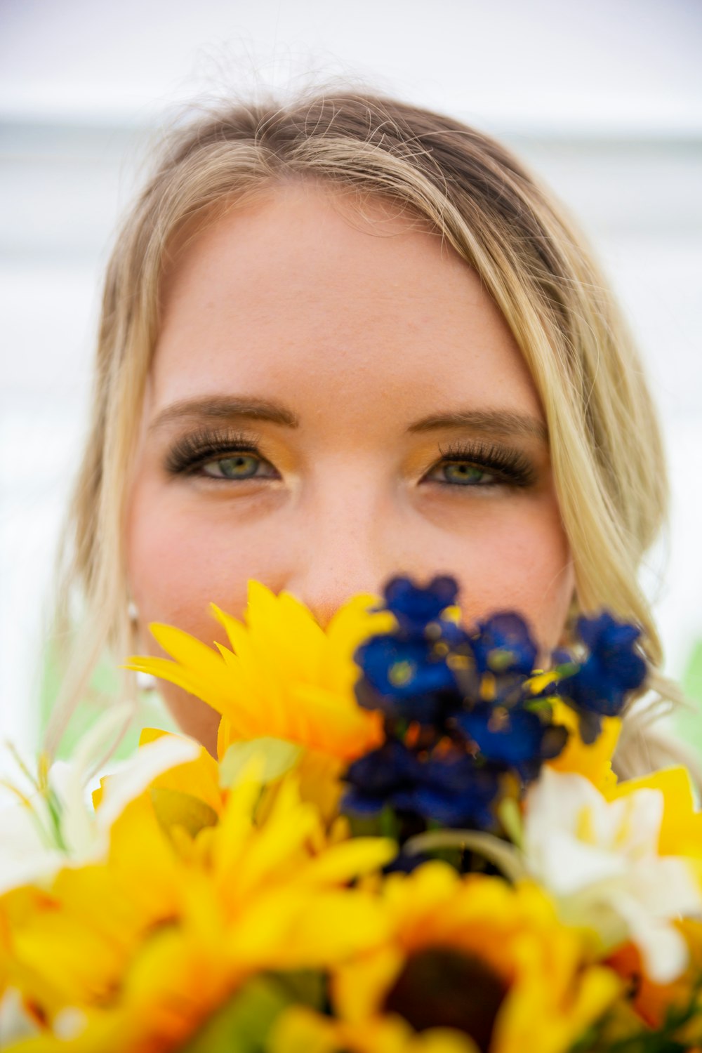 a woman holding a bouquet of sunflowers and blue flowers