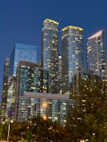 A cityscape featuring buildings with natural stone facades illuminated by evening lights.