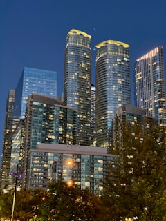 A cityscape featuring buildings with natural stone facades illuminated by evening lights.