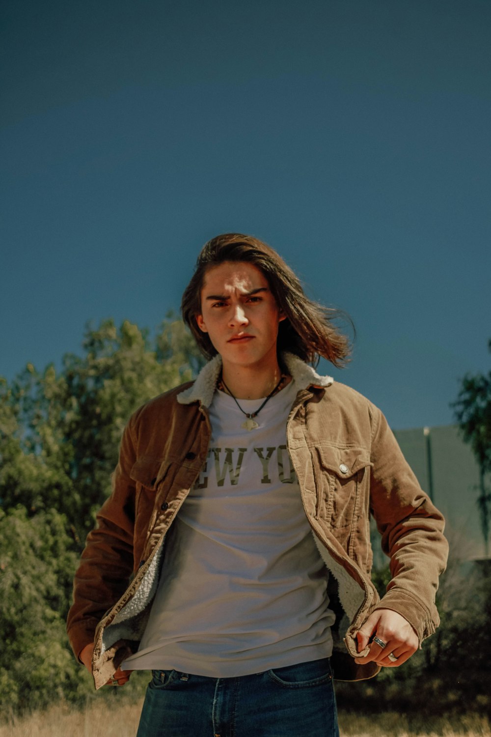 a man with long hair standing in a field