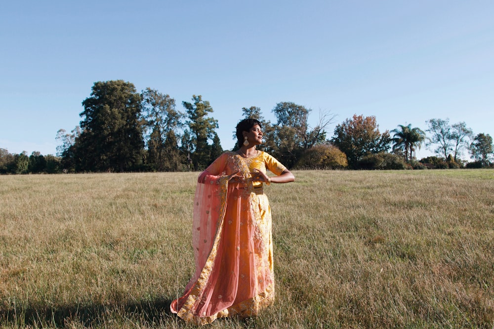 a woman in a yellow and orange dress standing in a field