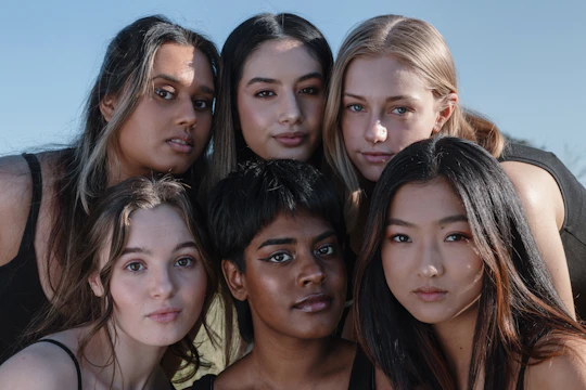 Close-up of diverse women smiling, showcasing healthy, natural hairstyles in a sunny outdoor setting.