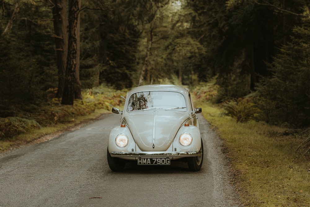 a white vw bug driving down a forest road