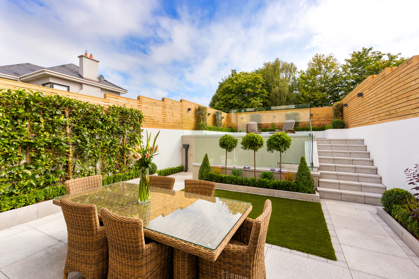 A split-level back garden with a pale porcelain patio, granite steps, a raised lawn and slatted fencing
