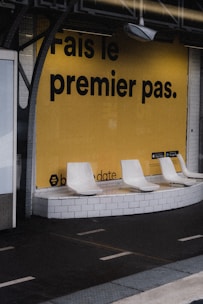 a row of white chairs sitting in front of a yellow wall
