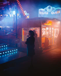 A night scene of a creepy carnival with distorted clown faces looming over a foggy midway.