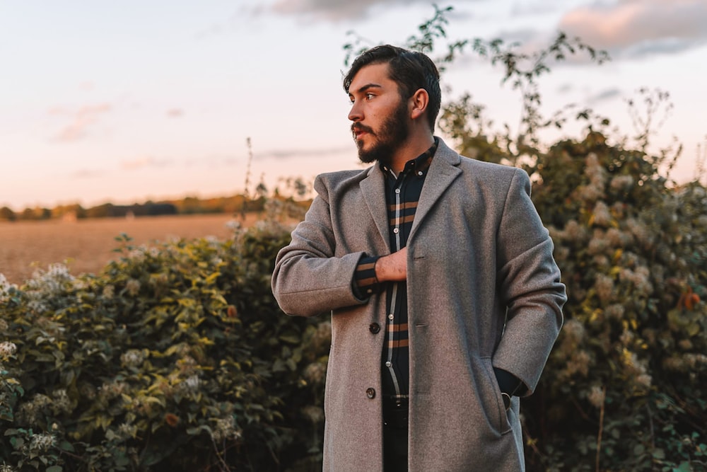a man standing in a field wearing a coat