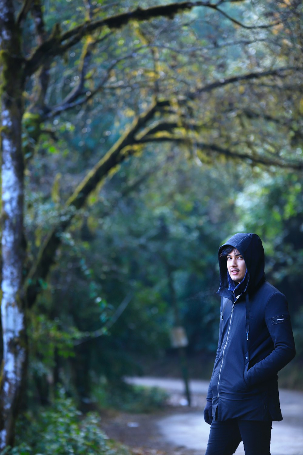 a woman in a black jacket is standing in the woods