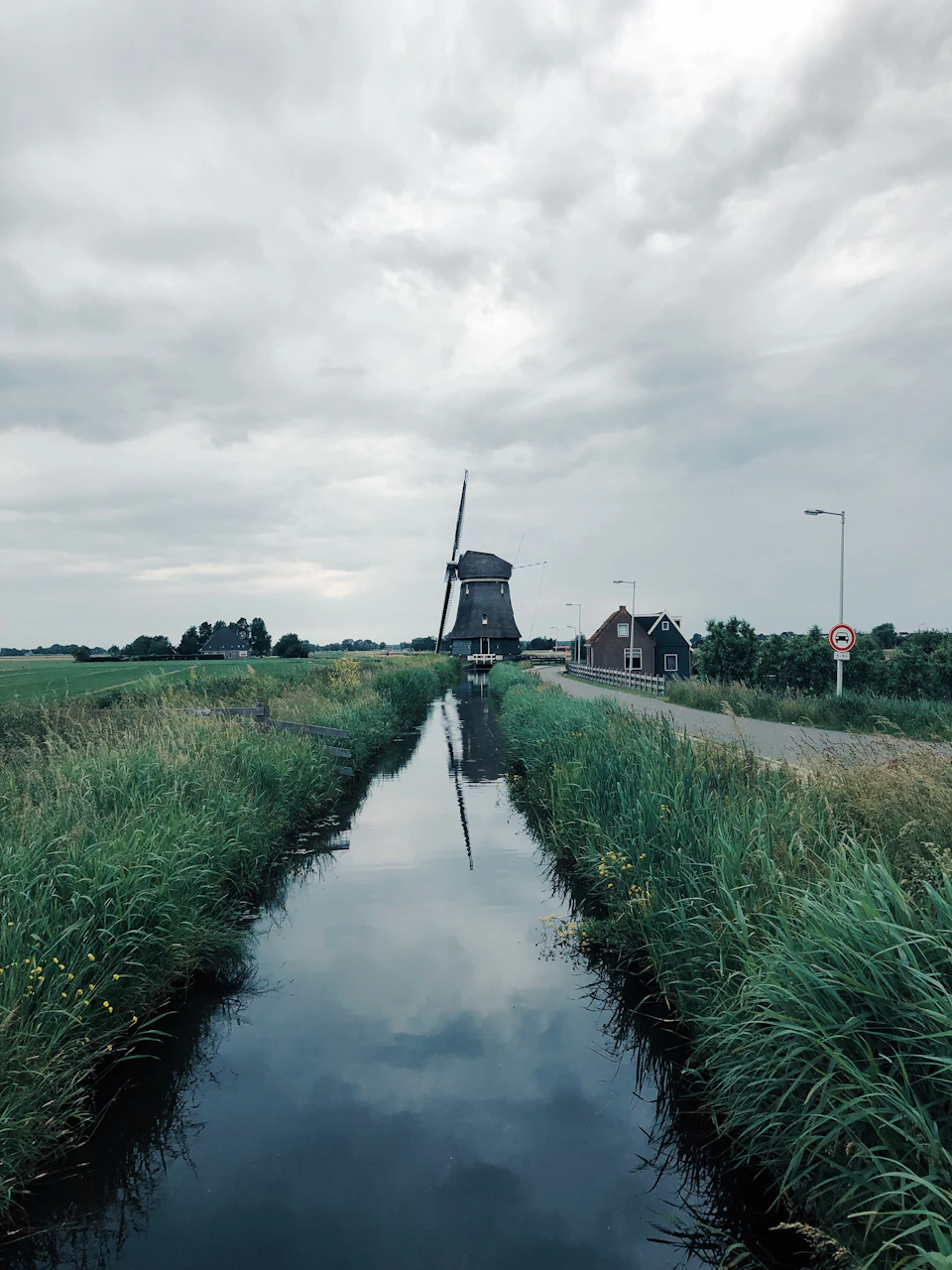 Molen aan het eind van een kaarsrecht kanaal, onder een zware lucht
