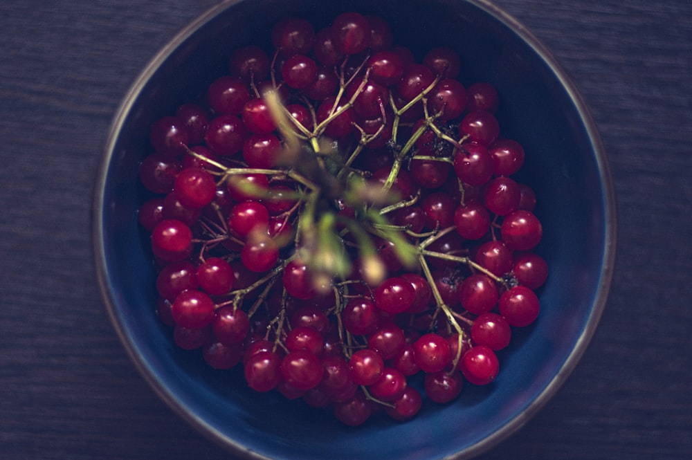 a blue bowl filled with red cherries on top of a wooden table
