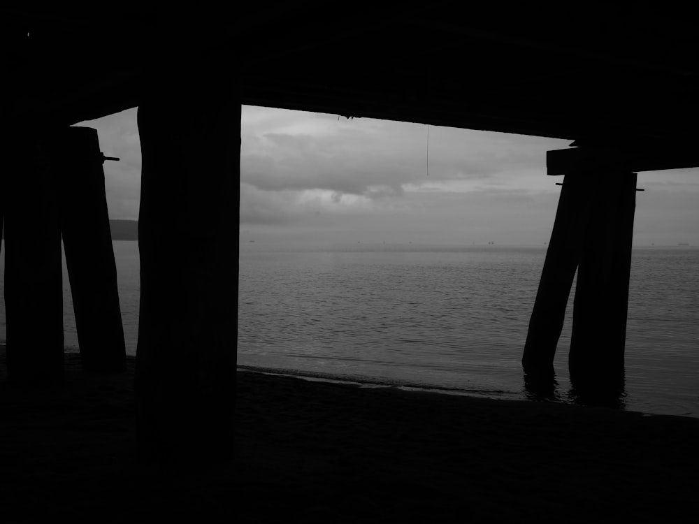 a black and white photo of the ocean under a pier