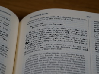 A close-up view of an open book displaying printed text on both visible pages. The book appears to be a Bible, with text formatted in columns and verse numbers. The focus is primarily on a section of text from a chapter, highlighting religious content.