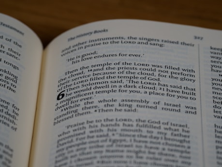 A close-up view of an open book displaying printed text on both visible pages. The book appears to be a Bible, with text formatted in columns and verse numbers. The focus is primarily on a section of text from a chapter, highlighting religious content.