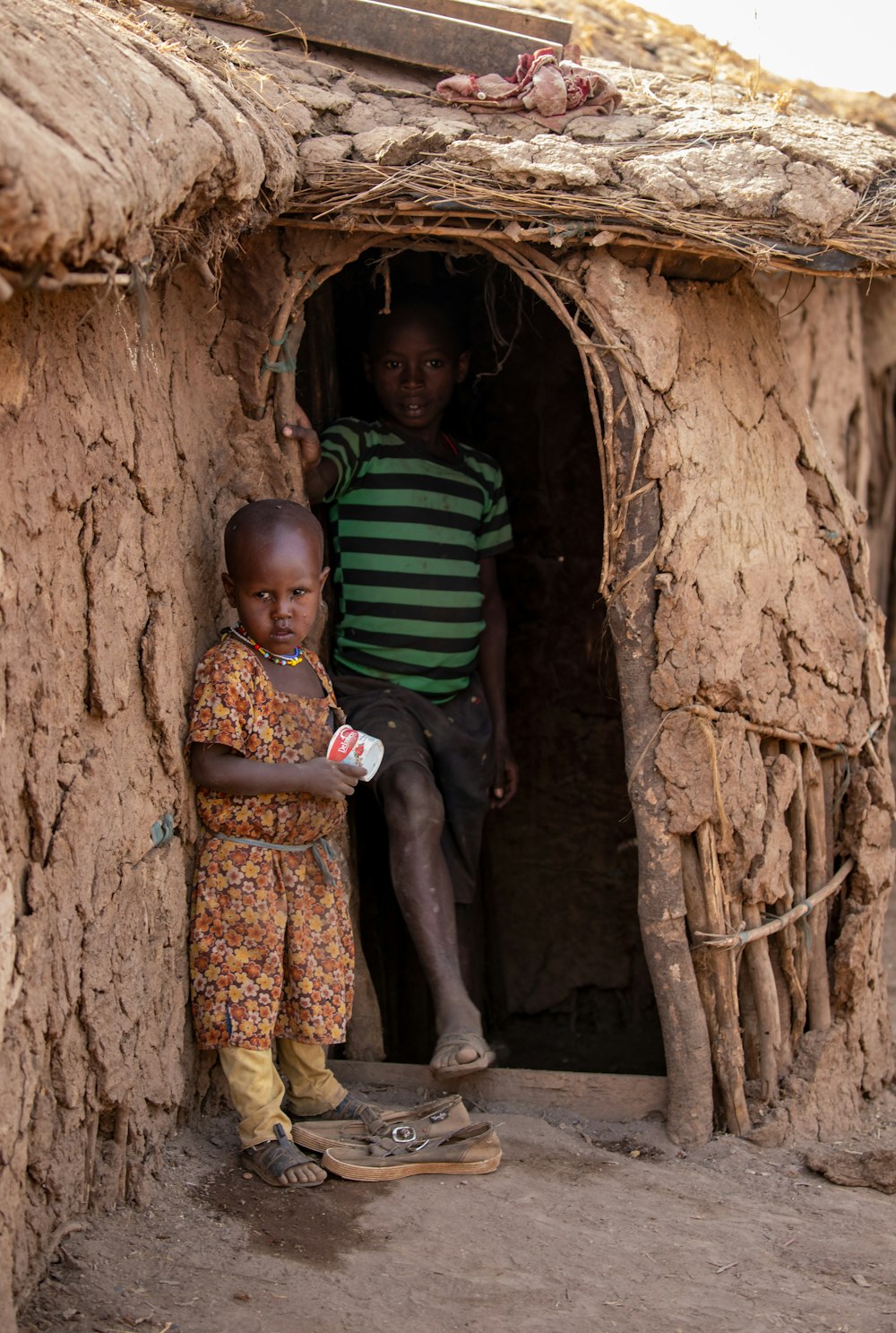 a couple of kids standing outside of a mud hut