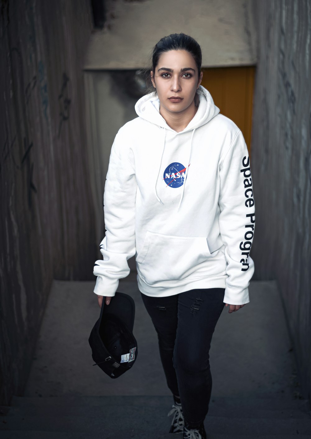 a woman in a white nasa hoodie walking down a hallway