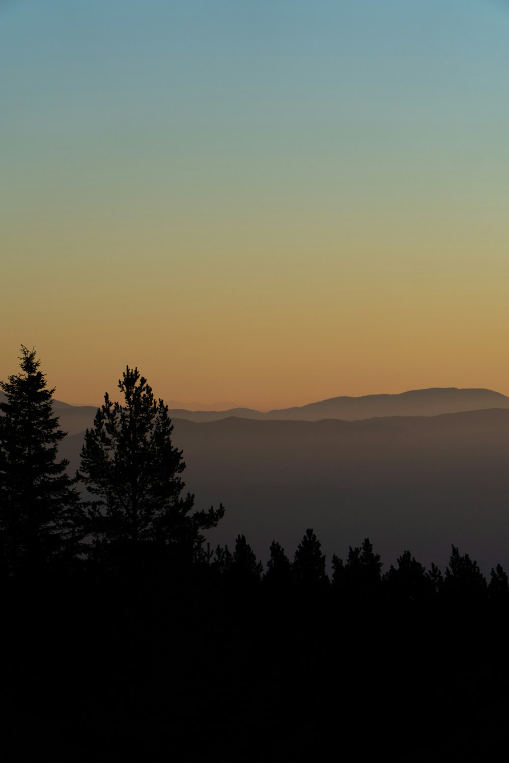 the sun is setting over the mountains and trees