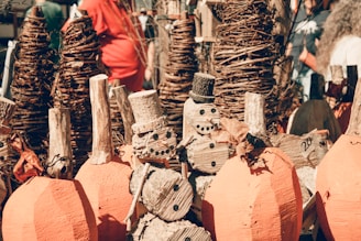 Wooden snowmen and pumpkins are crafted from logs and twigs, displayed among tall woven vine structures. The scene appears to be part of an outdoor craft or holiday market.