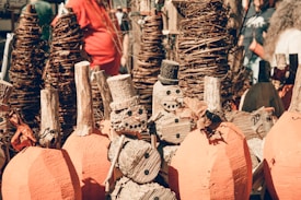 Wooden snowmen and pumpkins are crafted from logs and twigs, displayed among tall woven vine structures. The scene appears to be part of an outdoor craft or holiday market.
