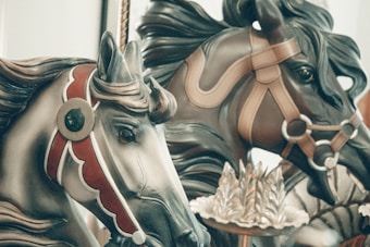 Ornate carousel horses featuring intricate details and decorative harnesses. The craftsmanship is highlighted with bold colors and elaborate patterns.