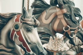 Ornate carousel horses featuring intricate details and decorative harnesses. The craftsmanship is highlighted with bold colors and elaborate patterns.