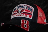 A baseball cap featuring the logo and colors of the Washington Capitals ice hockey team. The cap is predominantly black and red with the team's name and emblem embroidered on the front. The mesh back of the cap is red, and a large number 8 is stitched on the brim.