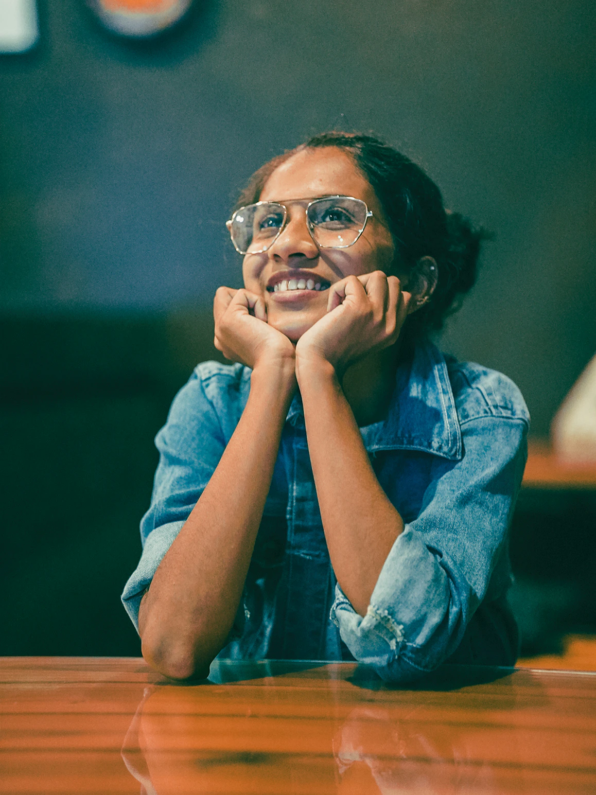 a woman sitting at a table with her hands on her chin