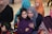 A group of people, including women and children, are gathered in what seems to be a social or family gathering. Several individuals are wearing colorful hijabs and winter clothing, suggesting a festive or warm environment.