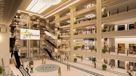 A spacious indoor shopping mall with multiple levels and ornate architectural details. Escalators and glass-fronted elevators connect the floors, while decorative lighting and large potted plants adorn the space. Shoppers can be seen walking or browsing in the store fronts on different levels. A large illuminated sign with the words 'Mall of Defence' is prominently displayed.